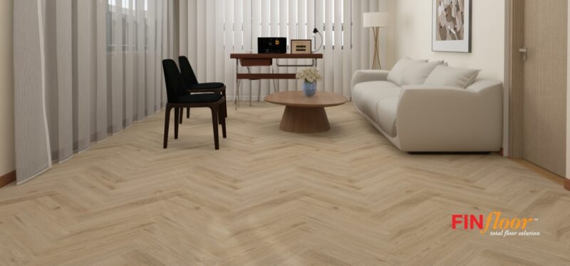 Herringbone flooring pattern in a warm oak wood-look finish, laid diagonally across a bright, modern living room